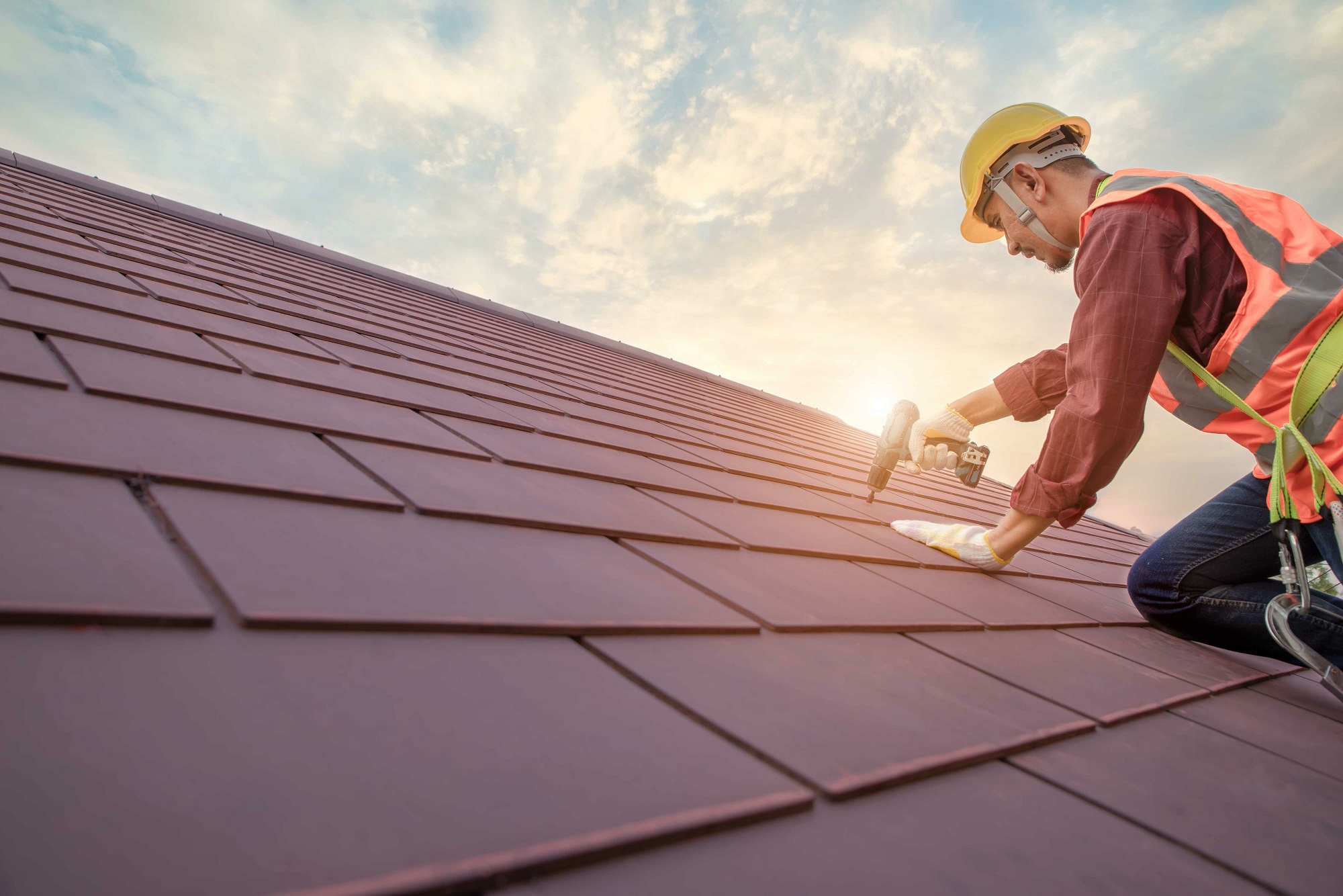 Roofer working in special protective work wear gloves, using air or pneumatic nail gun installing concrete or CPAC cement roofing tiles on top of the new roof under construction residential building